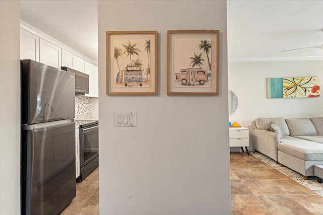 kitchen featuring stove, white cabinets, light stone countertops, stainless steel refrigerator, and light tile floors