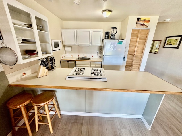 kitchen featuring white cabinetry, light wood-type flooring, white appliances, and kitchen peninsula