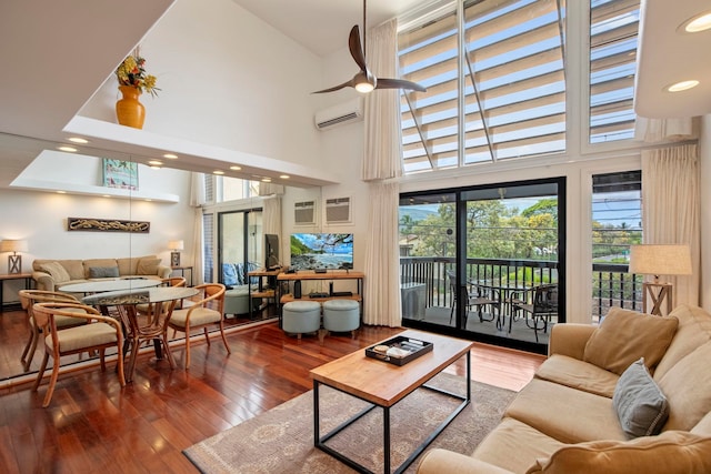 living room featuring a towering ceiling, hardwood / wood-style floors, a wall mounted AC, and a ceiling fan