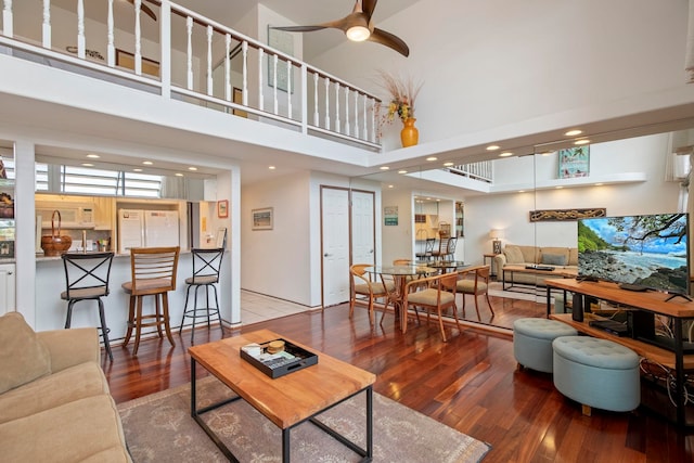 living room featuring wood finished floors, ceiling fan, recessed lighting, and a high ceiling