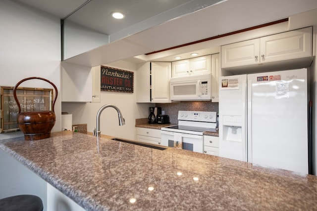 kitchen with dark stone counters, a sink, tasteful backsplash, white cabinetry, and white appliances