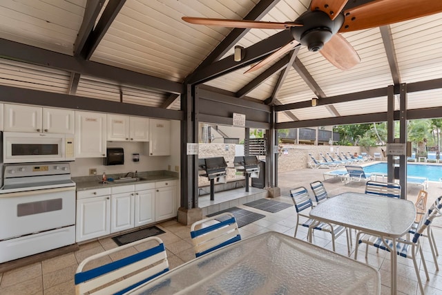 view of patio with a sink, a community pool, ceiling fan, an outdoor kitchen, and fence