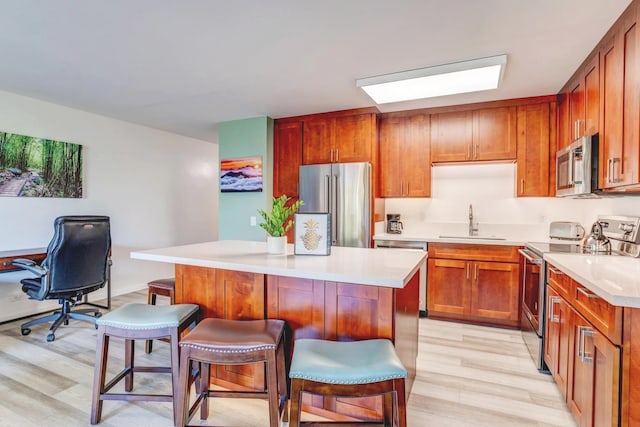 kitchen with appliances with stainless steel finishes, sink, a kitchen bar, a kitchen island, and light hardwood / wood-style floors