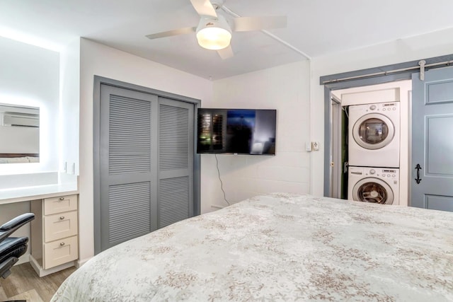 bedroom with light hardwood / wood-style flooring, ceiling fan, stacked washer / drying machine, a closet, and built in desk