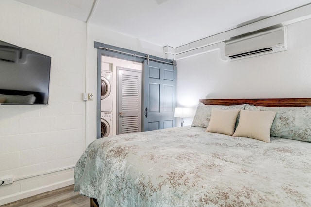 bedroom with wood-type flooring, an AC wall unit, stacked washer and clothes dryer, and a barn door