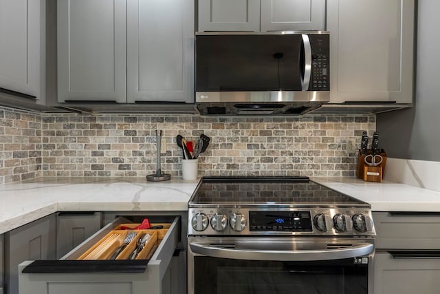 480 Kenolio Rd Unit 24-202, Kihei, HI 96753 - kitchen featuring appliances with stainless steel finishes, decorative backsplash, gray cabinetry, and light stone countertops
