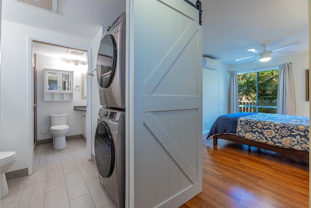 clothes washing area featuring a wall mounted air conditioner, a textured ceiling, ceiling fan, a barn door, and stacked washer and dryer