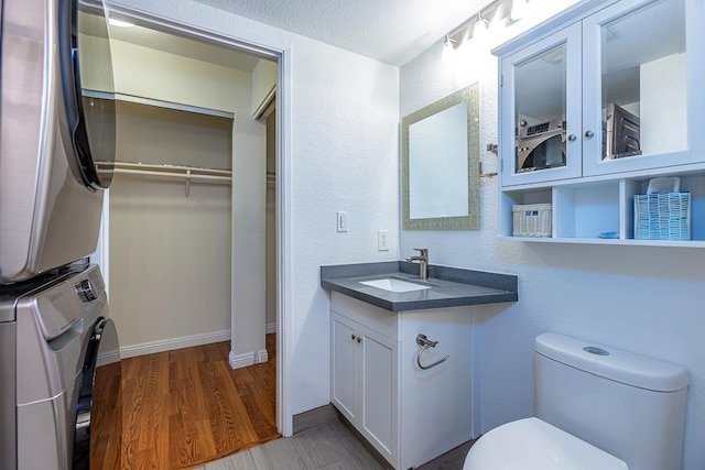 bathroom featuring stacked washer and dryer, a textured ceiling, toilet, vanity, and hardwood / wood-style flooring