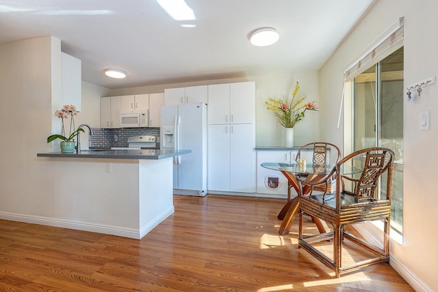 kitchen with kitchen peninsula, dark hardwood / wood-style flooring, white appliances, and white cabinetry