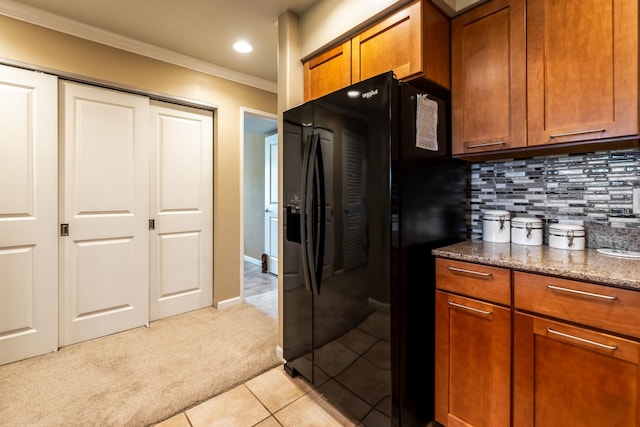kitchen with backsplash, dark stone counters, ornamental molding, black fridge, and light carpet
