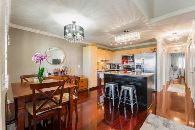 kitchen with dark wood-type flooring, light brown cabinetry, a center island, a notable chandelier, and stainless steel appliances