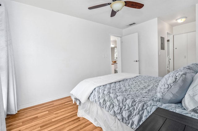 bedroom featuring ensuite bath, electric panel, light hardwood / wood-style flooring, and ceiling fan