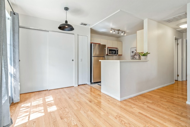 kitchen with kitchen peninsula, light wood-type flooring, stainless steel appliances, white cabinets, and hanging light fixtures