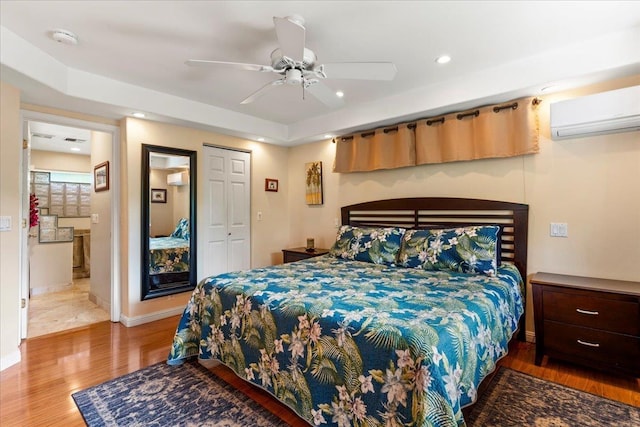 bedroom featuring ensuite bathroom, ceiling fan, wood-type flooring, a closet, and a wall unit AC