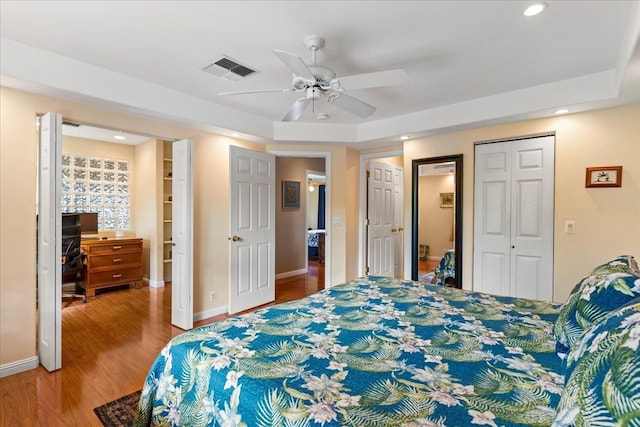 bedroom featuring a raised ceiling, ceiling fan, and light wood-type flooring