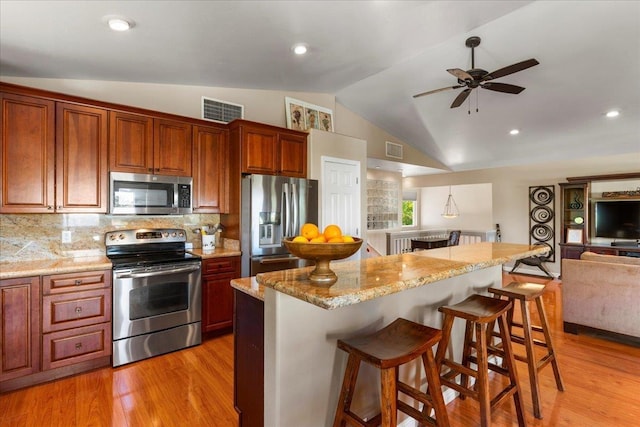 kitchen with vaulted ceiling, a kitchen breakfast bar, backsplash, a kitchen island, and appliances with stainless steel finishes