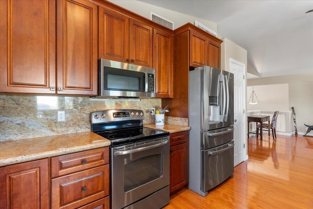 kitchen featuring stainless steel appliances, light stone counters, decorative backsplash, light hardwood / wood-style flooring, and lofted ceiling