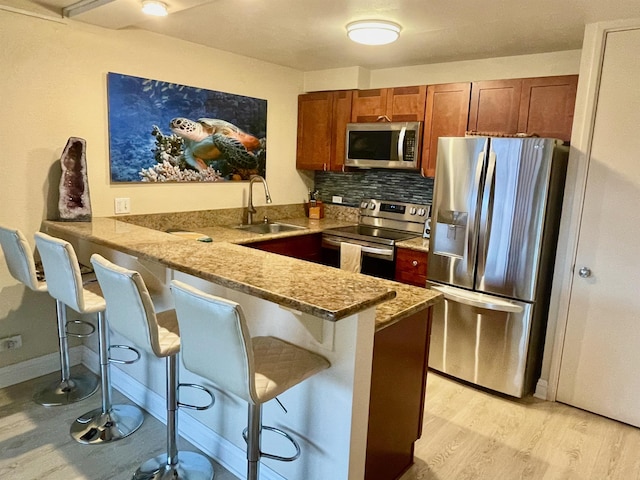 kitchen featuring brown cabinets, a sink, stainless steel appliances, backsplash, and a peninsula