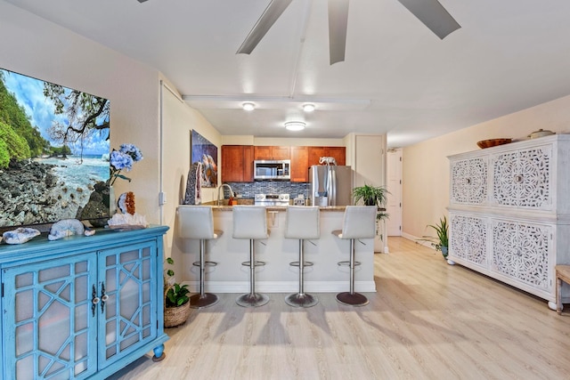 kitchen featuring appliances with stainless steel finishes, light wood-style floors, brown cabinets, and a peninsula