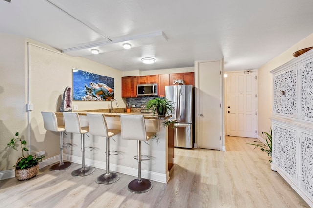 kitchen with a kitchen breakfast bar, light wood-style floors, stainless steel appliances, and a peninsula