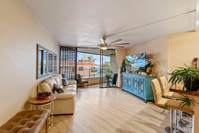 living area with wood finished floors, a ceiling fan, a wall of windows, and a textured wall