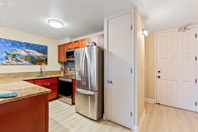 kitchen featuring a sink, stainless steel appliances, brown cabinetry, light wood-type flooring, and light stone counters