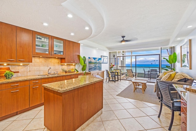 kitchen with sink, light tile patterned floors, light stone counters, a textured ceiling, and a kitchen island