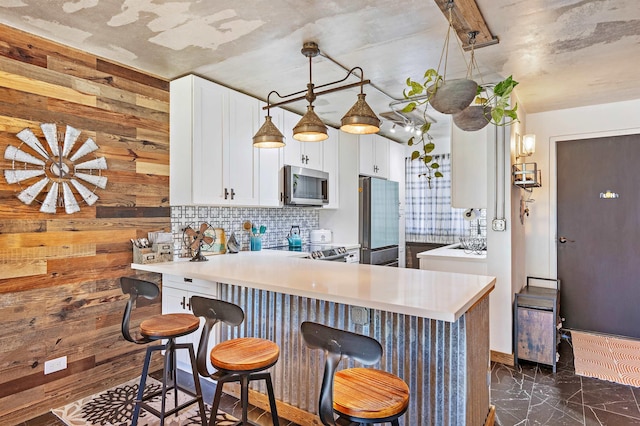 kitchen with a peninsula, white cabinets, a kitchen breakfast bar, appliances with stainless steel finishes, and backsplash