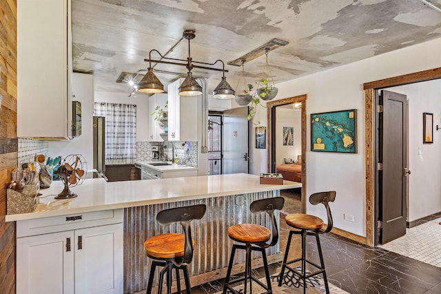 kitchen with a peninsula, white cabinetry, a kitchen breakfast bar, light countertops, and decorative backsplash