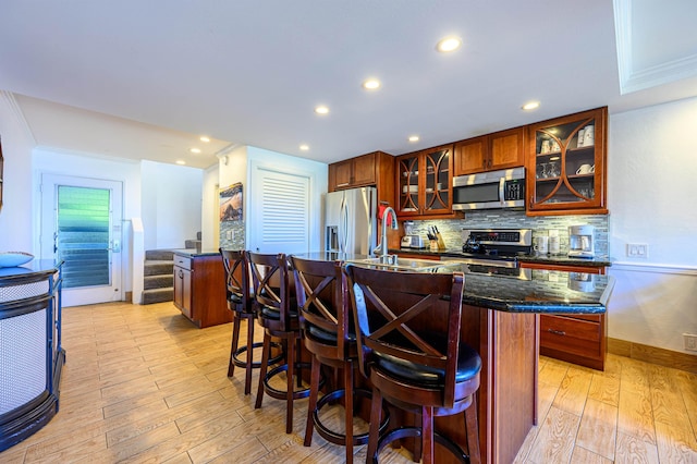 kitchen with sink, a center island with sink, light wood-type flooring, and appliances with stainless steel finishes