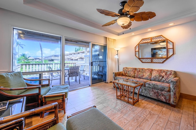 living room with light hardwood / wood-style floors, a raised ceiling, ornamental molding, and ceiling fan