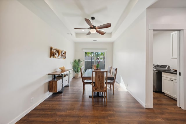 dining space featuring a tray ceiling, washer / clothes dryer, dark wood finished floors, baseboards, and ceiling fan