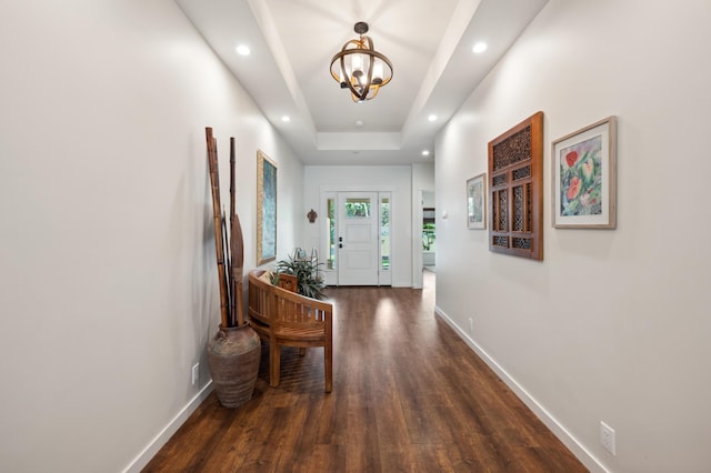 interior space featuring a notable chandelier, a raised ceiling, baseboards, and dark wood-style flooring