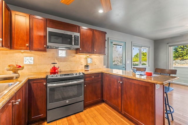 kitchen featuring kitchen peninsula, stainless steel appliances, a breakfast bar area, and light hardwood / wood-style flooring