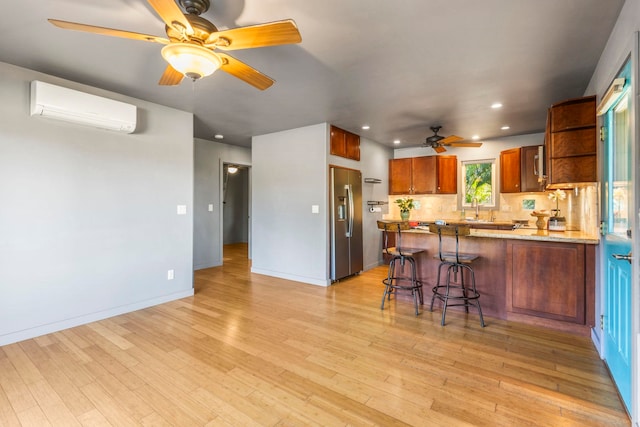 kitchen featuring sink, stainless steel refrigerator with ice dispenser, kitchen peninsula, a wall mounted AC, and light wood-type flooring