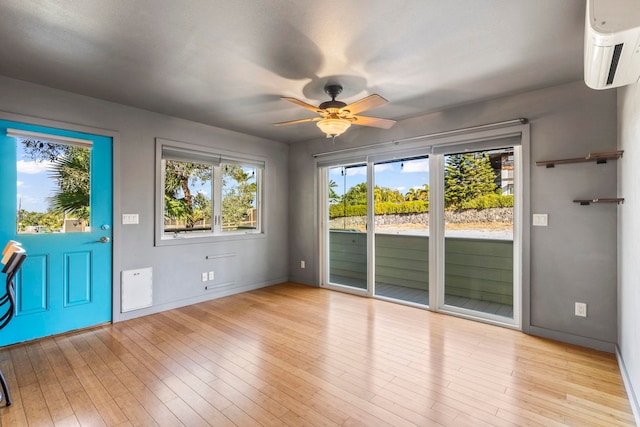 interior space with a wall mounted AC, light hardwood / wood-style floors, and ceiling fan