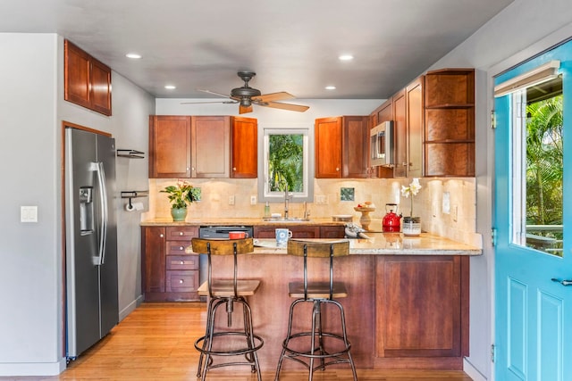 kitchen featuring light stone countertops, sink, ceiling fan, stainless steel appliances, and kitchen peninsula