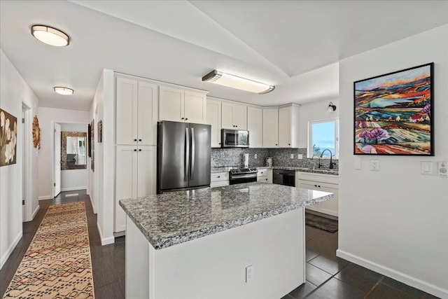 kitchen with white cabinets, appliances with stainless steel finishes, light stone counters, a sink, and backsplash