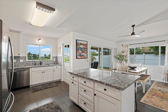 kitchen with ceiling fan, a kitchen island, appliances with stainless steel finishes, a sink, and backsplash