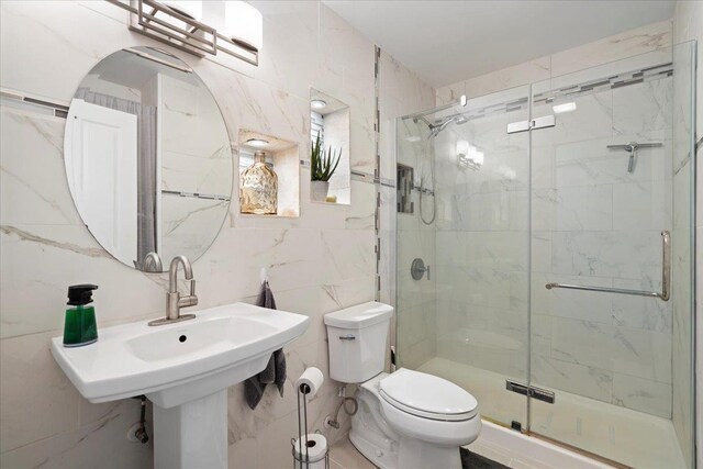 bathroom featuring toilet, tile walls, a stall shower, and a sink