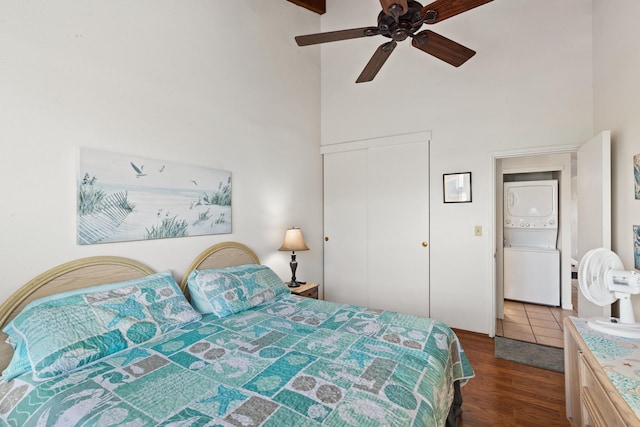 bedroom featuring a towering ceiling, dark hardwood / wood-style flooring, a closet, stacked washer / drying machine, and ceiling fan