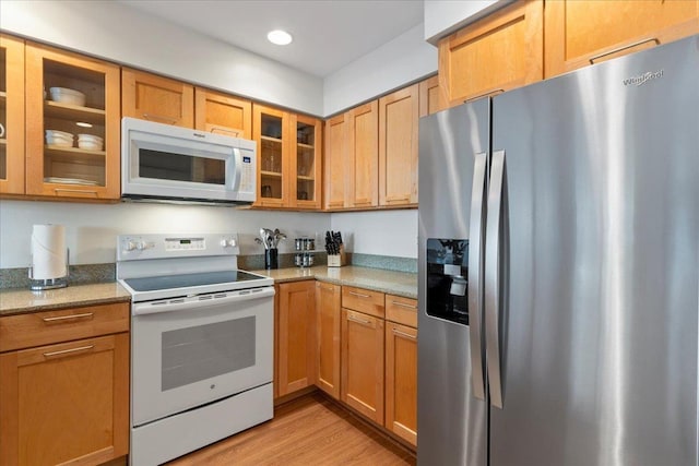 kitchen with white appliances, light stone countertops, and light wood-type flooring