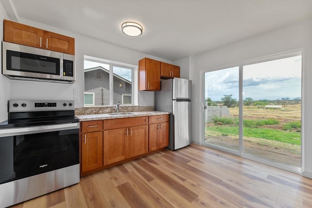 495 Kaiolohia St, Kihei, HI 96753 - kitchen featuring light stone counters, stainless steel appliances, brown cabinets, light wood finished floors, and a sink