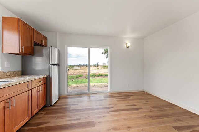 495 Kaiolohia St, Kihei, HI 96753 - kitchen featuring brown cabinets, light wood-style floors, freestanding refrigerator, baseboards, and light stone countertops
