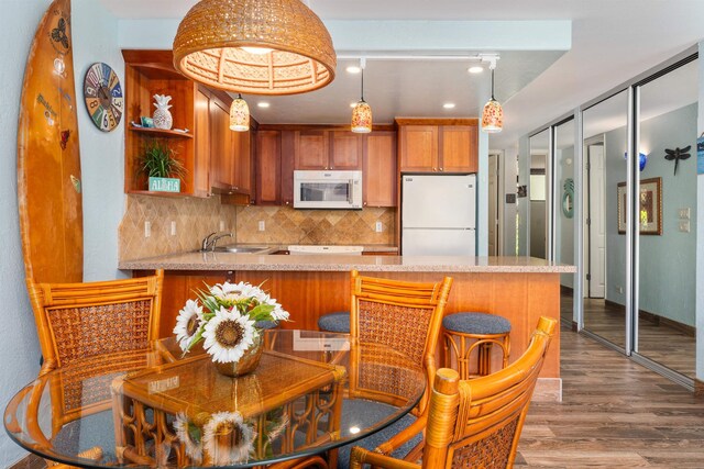 kitchen featuring white appliances, hanging light fixtures, decorative backsplash, sink, and kitchen peninsula