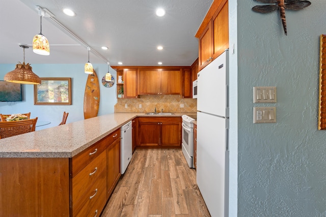 kitchen featuring kitchen peninsula, pendant lighting, sink, tasteful backsplash, and white appliances