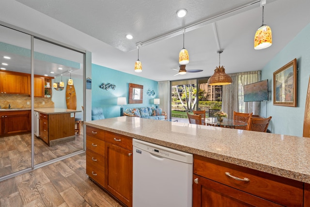 kitchen featuring light stone countertops, white dishwasher, hardwood / wood-style flooring, pendant lighting, and backsplash