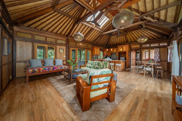 living area with a skylight, light hardwood / wood-style floors, wood walls, and high vaulted ceiling