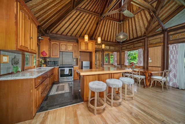 kitchen with high vaulted ceiling, stainless steel appliances, light hardwood / wood-style flooring, and a center island