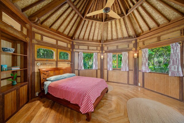 bedroom featuring high vaulted ceiling, ceiling fan, wood walls, and multiple windows